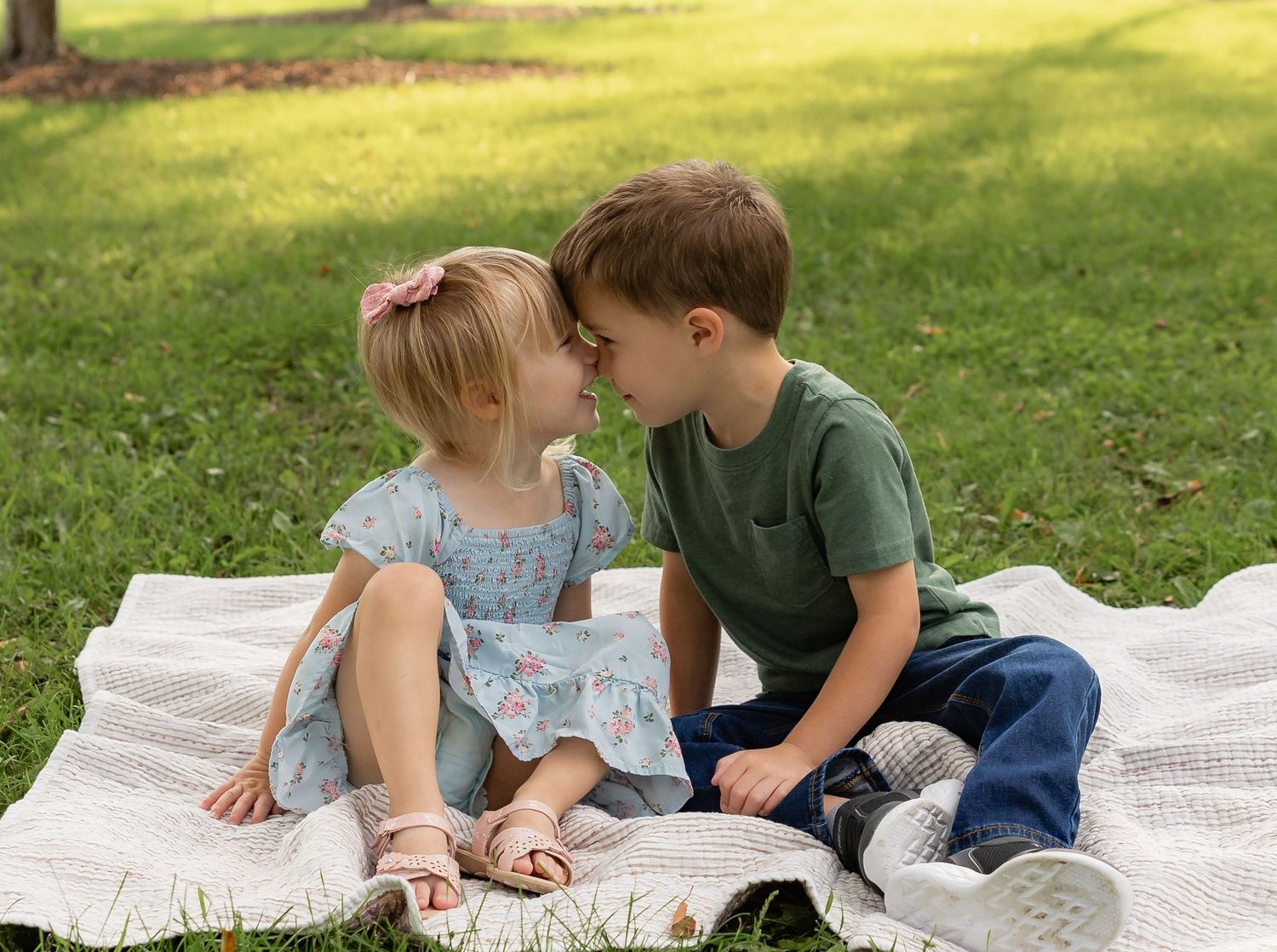Two children lying on a white blanket outdoors wearing casual clothes and making playful expressions.