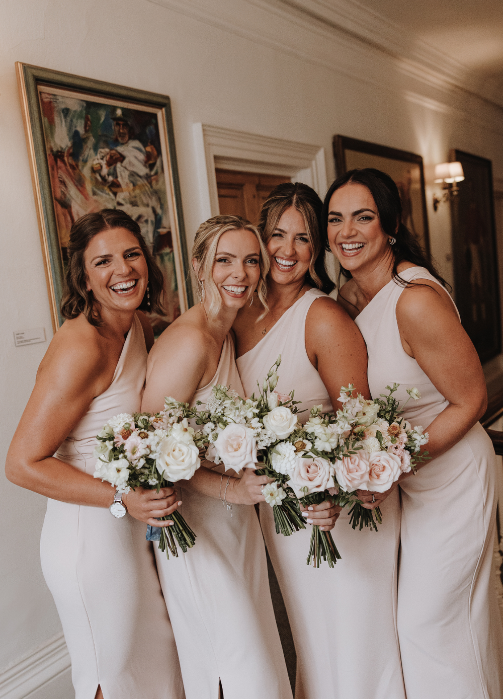 Bridesmaid's in elegant peach dresses hold matching blush and white floral bouquets while posing together at Deer Park Honiton
