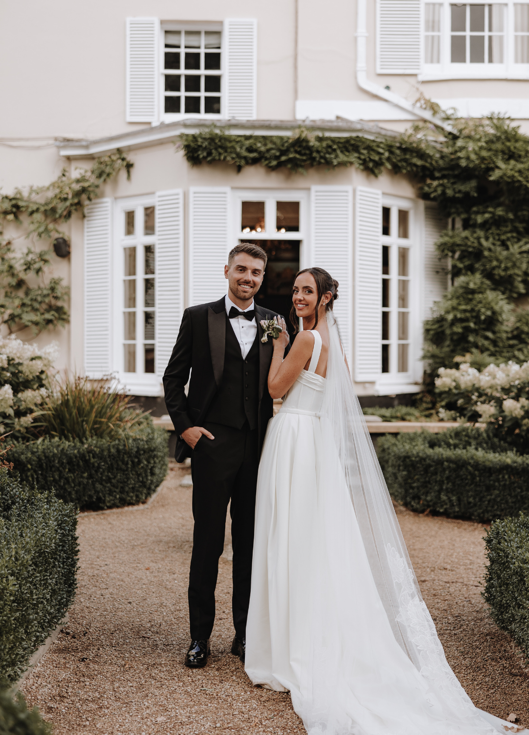 A wedding couple shares a romantic moment on a gravel path outside Deer Park Country House with shuttered windows.