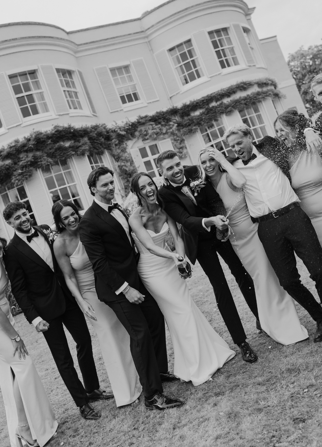 A wedding party in formal attire poses for a playful sequence of black and white photos outside an elegant building.