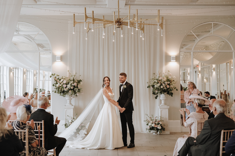 A series of elegant wedding ceremony photos showing white decor, floral arrangements, and guests at Deer Park Honiton.