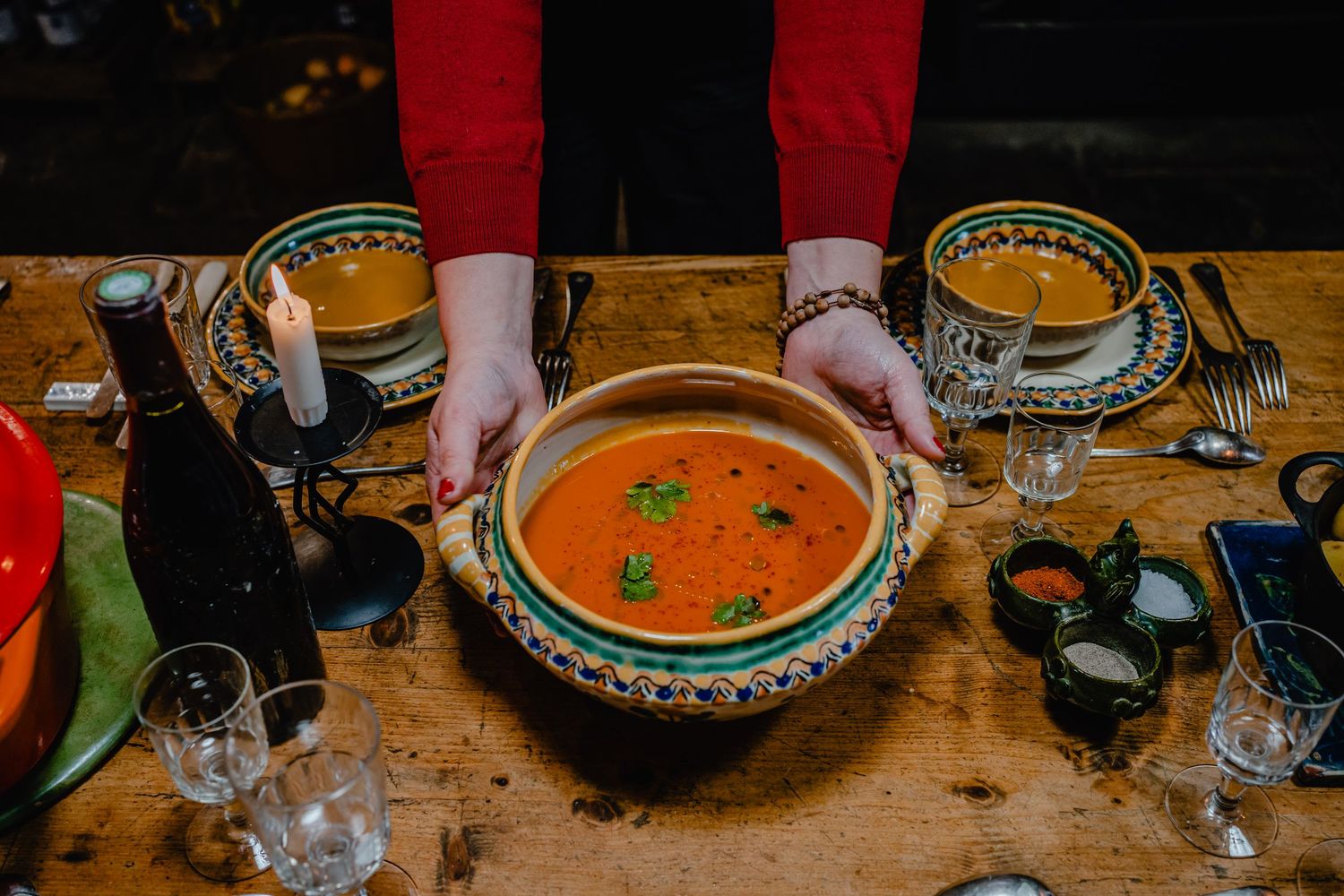 Several bowls of vibrant orange soup garnished with fresh herbs sit on a rustic wooden table.