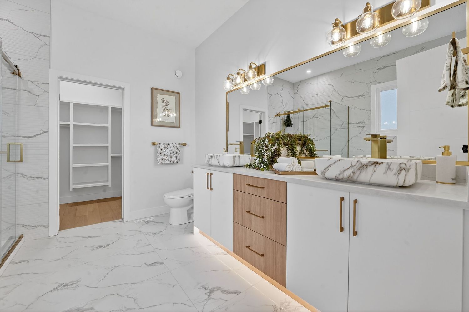 Luxurious bathroom featuring marble tiles, modern fixtures and bright white cabinetry.