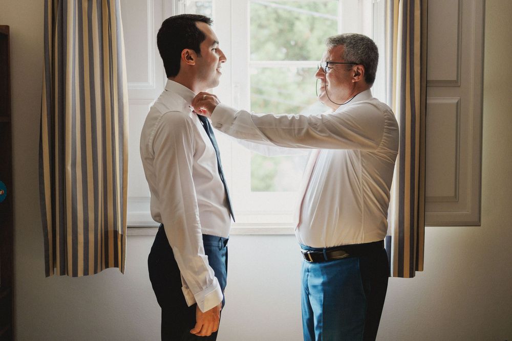 Two people stand by a window in formal attire while having an animated conversation.