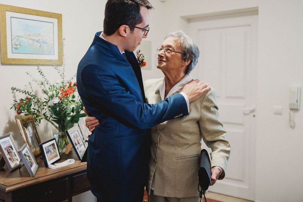 Two people share an emotional embrace in a room with framed artwork and flowers on display.