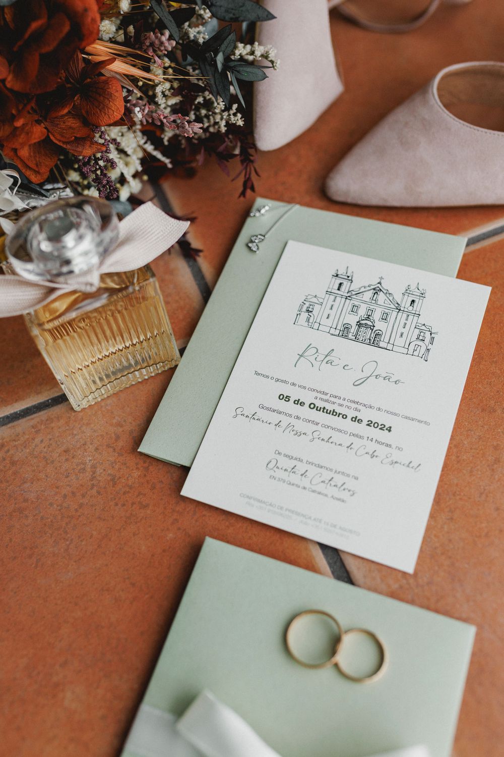 Wedding invitation cards with hand-drawn church illustration and rings on a terracotta surface with floral decor.