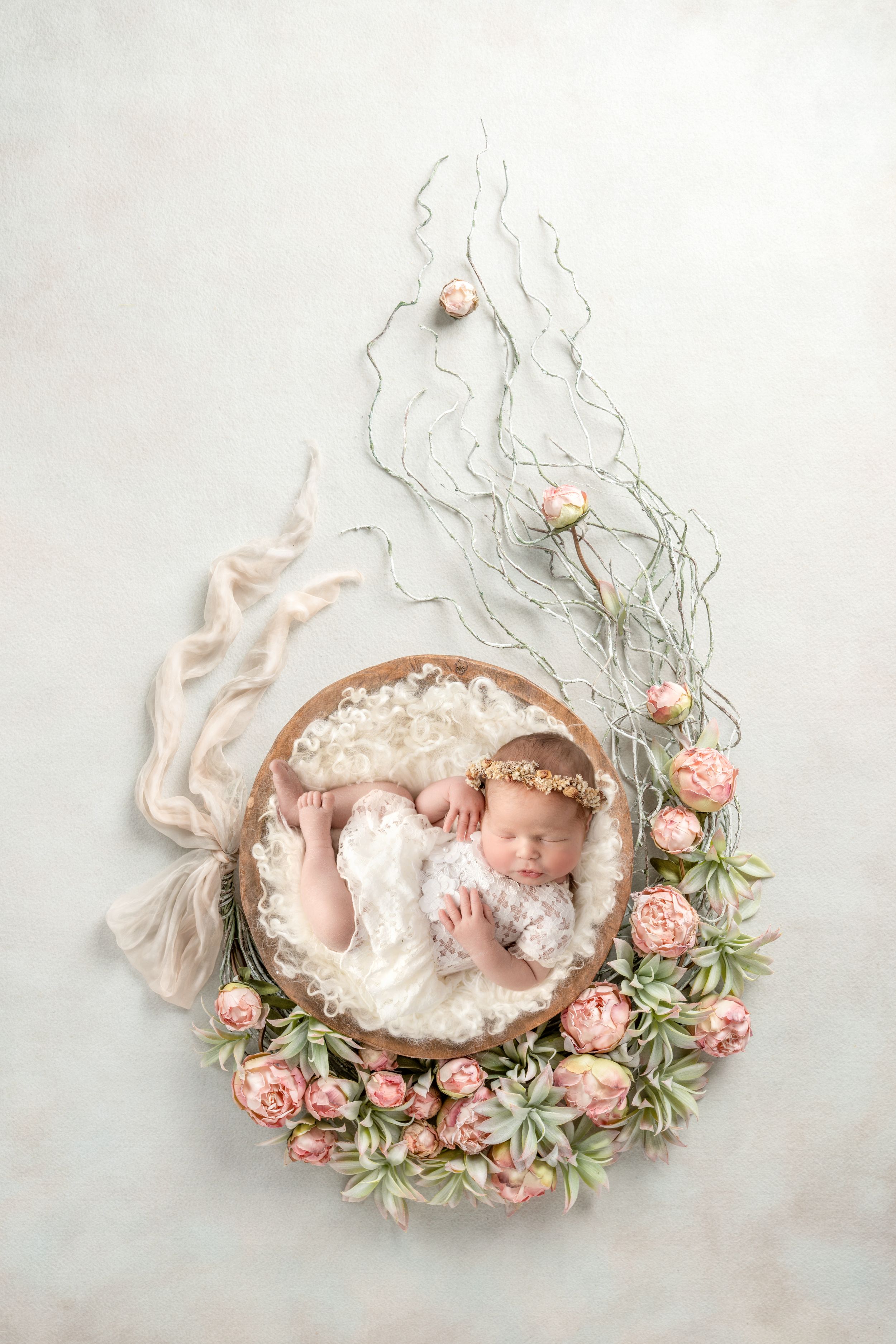 Newborn baby sleeping in wooden bowl with pink roses and floral crown on white background. Newborn Baby Photographer Cork