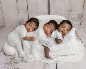Three sleeping newborn triplets dressed in white outfits posed together in a soft white couch prop. Newborn Photographer Cork