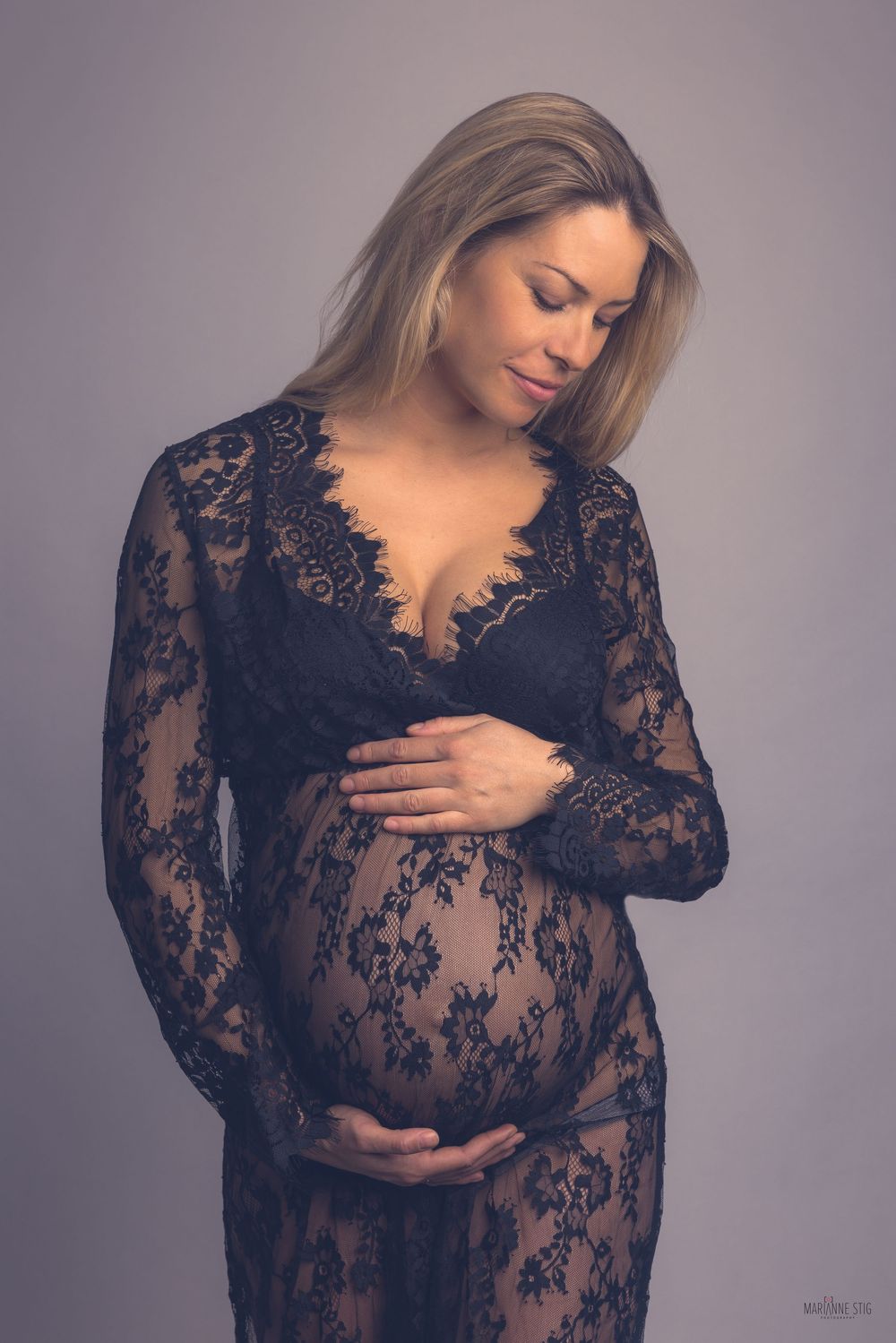 Elegant maternity photo featuring a black lace gown against a gray background in a soft, romantic style.