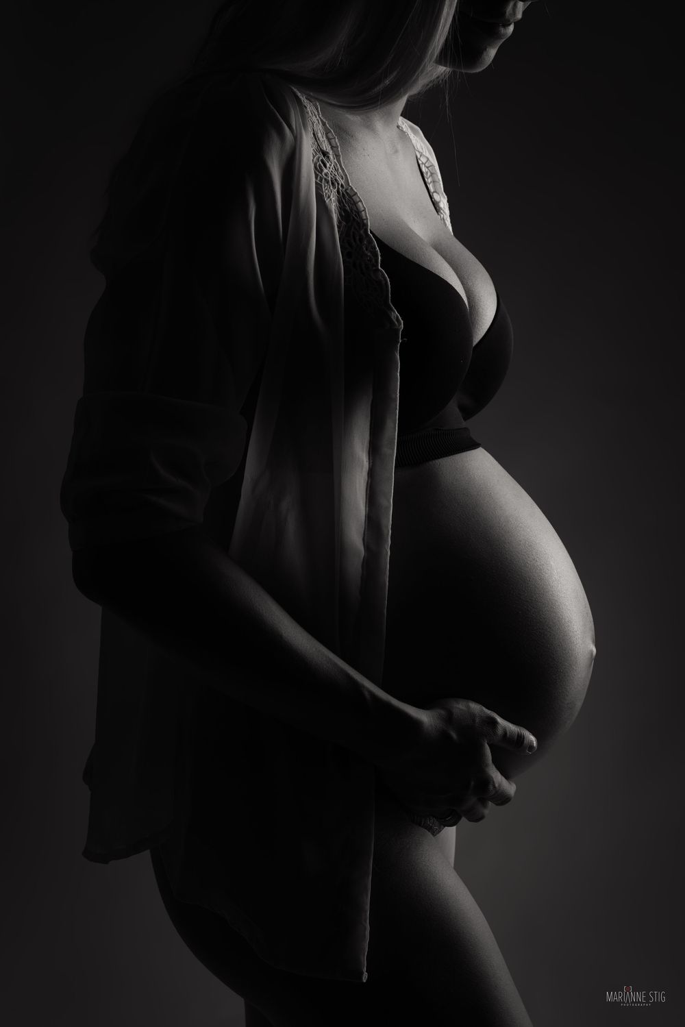 A series of black and white maternity silhouettes showing a pregnant belly from different artistic angles in low key lighting.