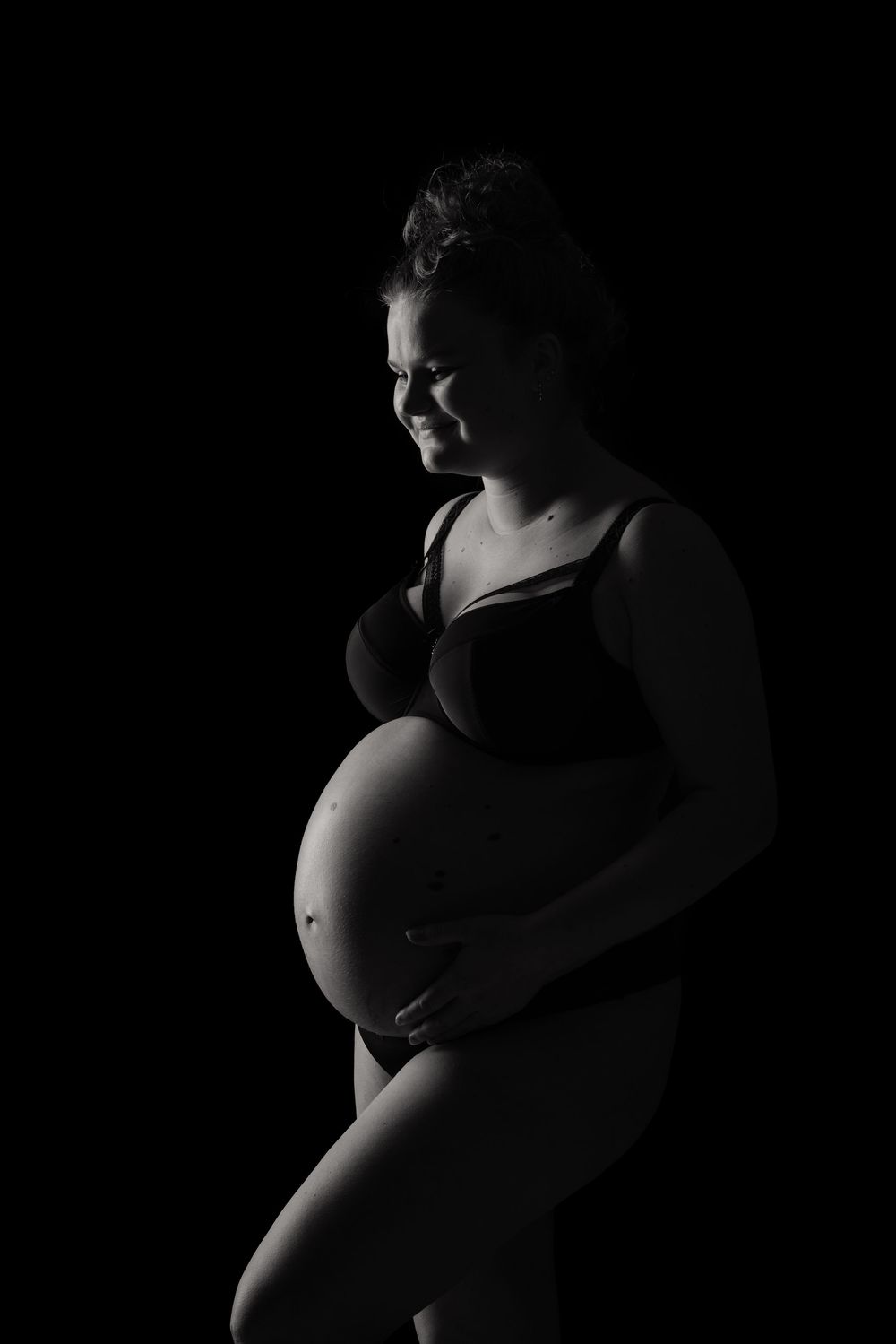 Black and white silhouette of a pregnant woman cradling her baby bump against a dark background.