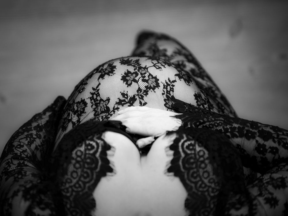 Black and white close-up of a pregnant belly draped in elegant lace fabric, showcasing intricate floral patterns.