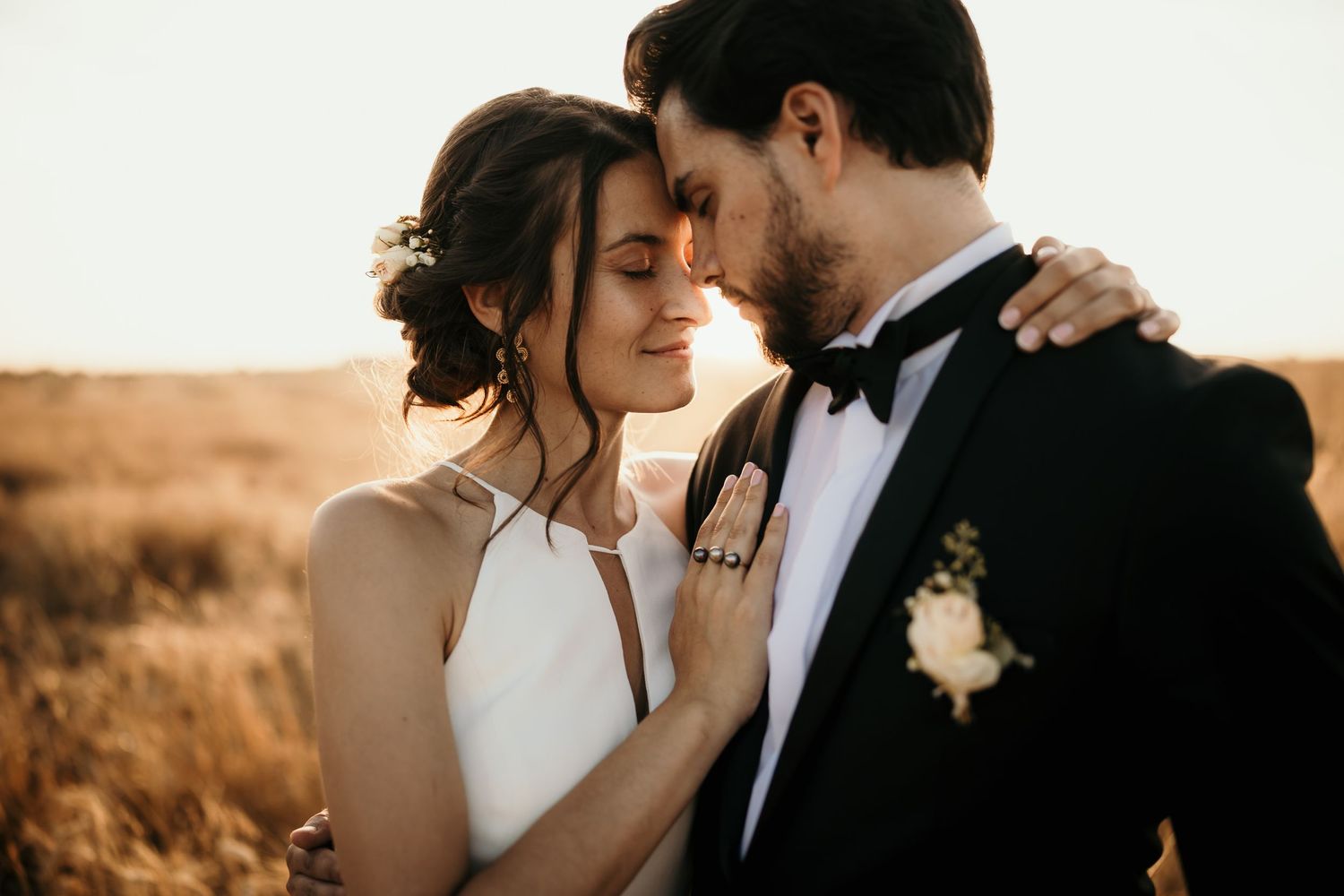 An intimate moment between a bride and groom in formal attire against a warm landscape.