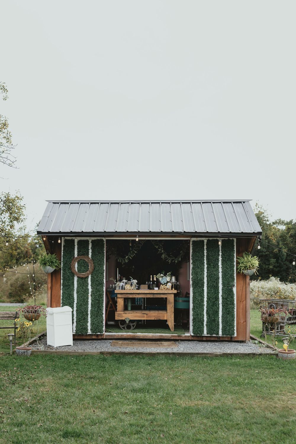 Modern outdoor pavilion with green glass panels and wooden bench seating set in a grassy meadow landscape.