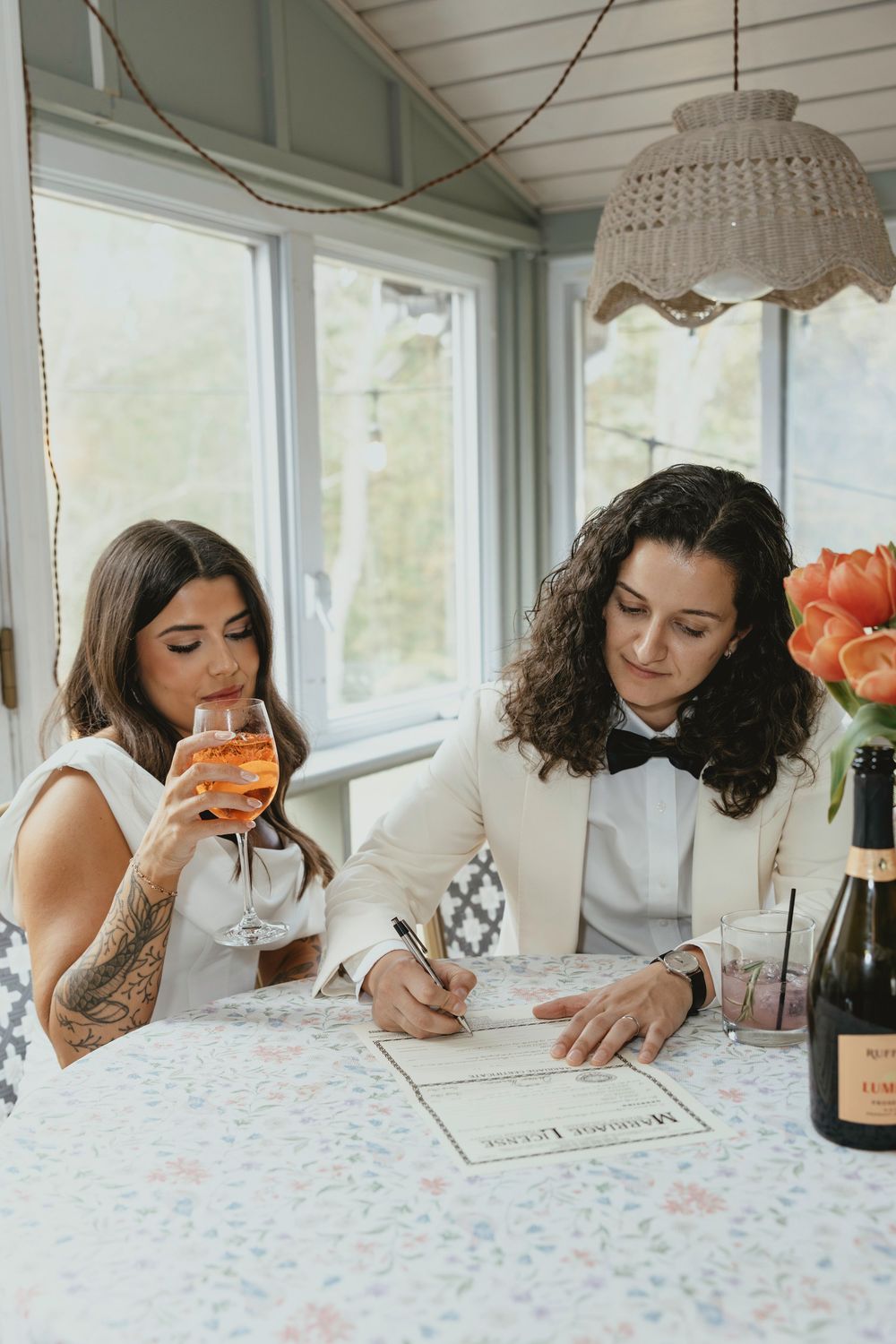 A series of four photos showing someone signing documents on a white tablecloth with champagne and flowers nearby.