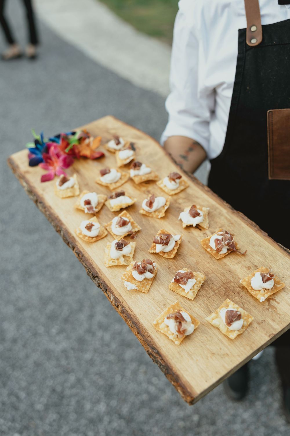 Elegant appetizers displayed on a rustic wooden serving board with colorful edible flowers.