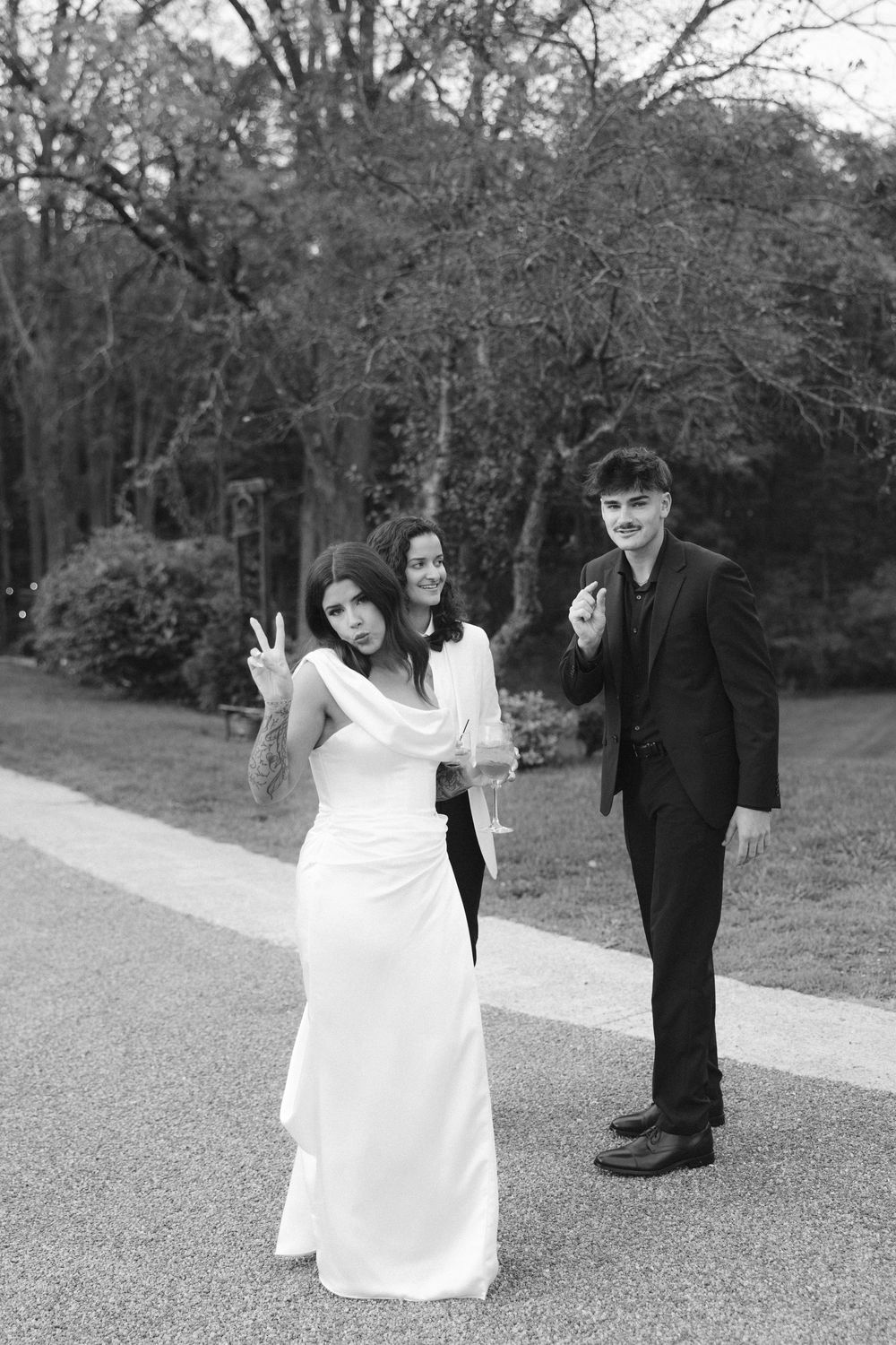 A black and white photo of a wedding party making peace signs on a garden path.