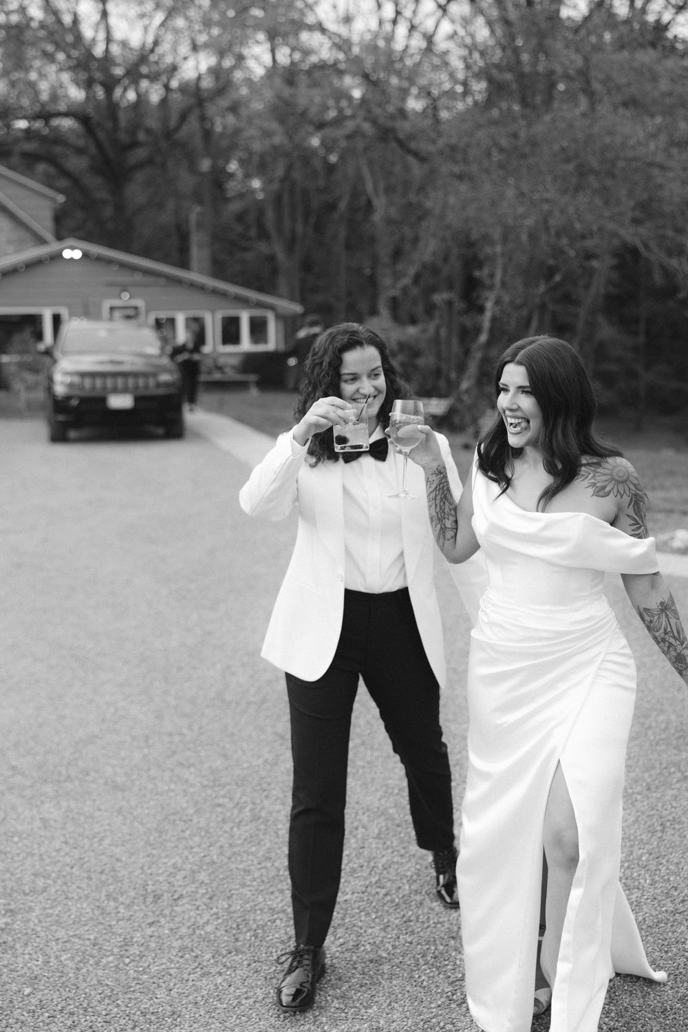 Two people in black and white formal attire dance and laugh together playfully in an outdoor setting.
