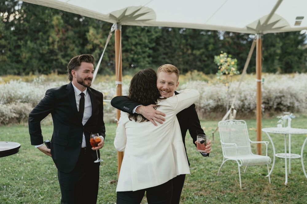 A joyful moment captured at an outdoor wedding ceremony with white chairs and a tent canopy in a garden setting.
