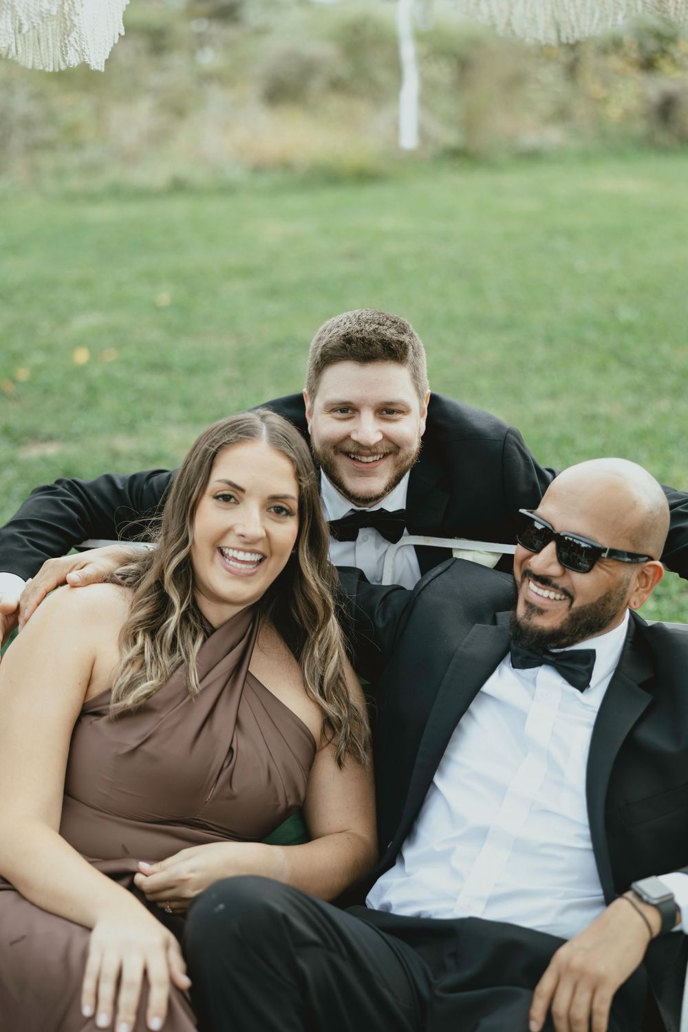 A group relaxes and laughs together while laying in grass wearing formal attire.