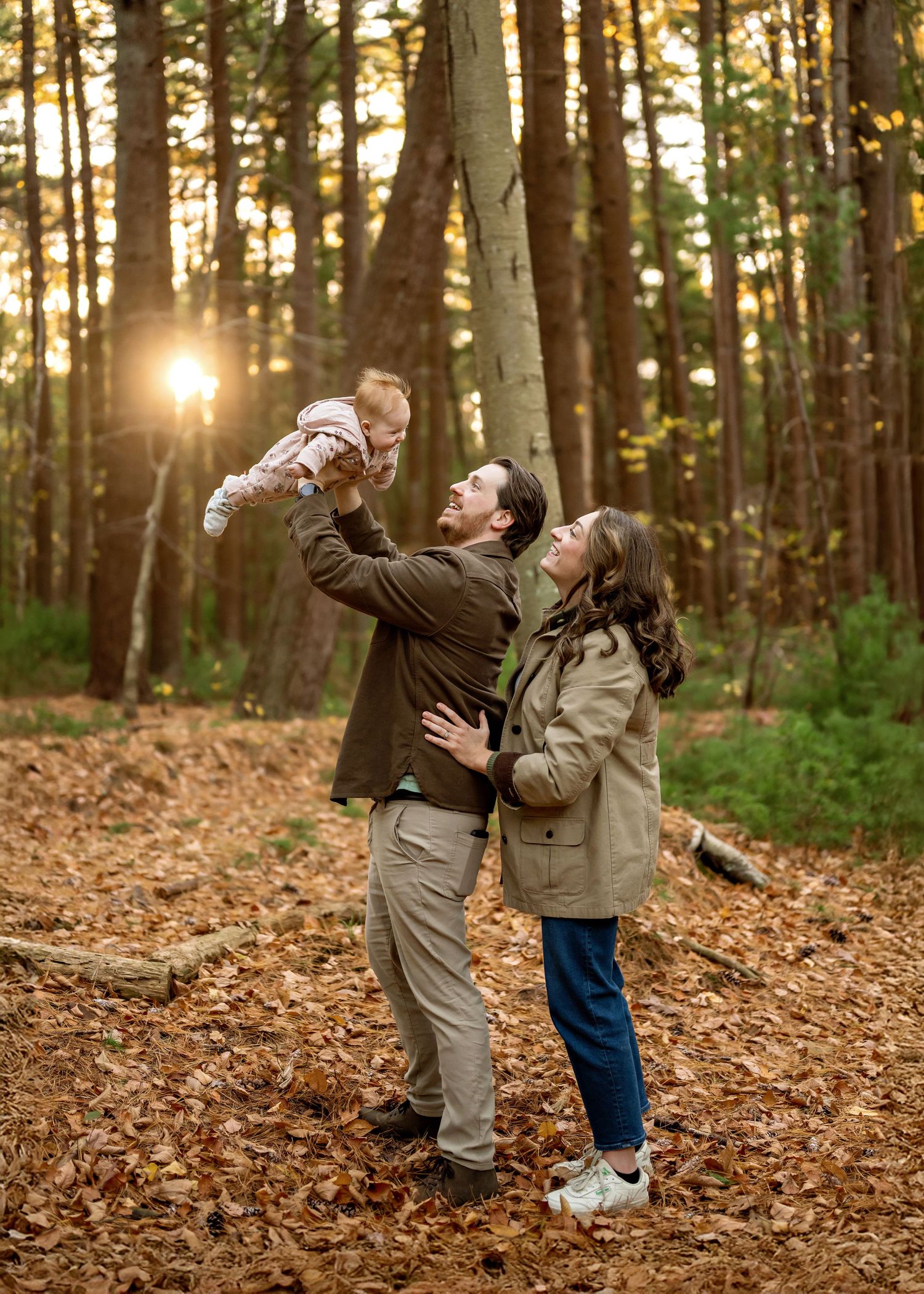 Family enjoying a playful moment together in an autumn forest with golden sunlight streaming through the trees.