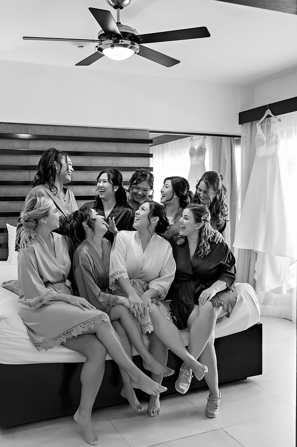 A group in matching robes sits together on a couch in a bright room with ceiling fans, creating a joyful atmosphere.