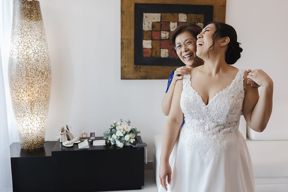 A bride in a white lace wedding dress poses with a natural, joyful expression in an elegant indoor setting.