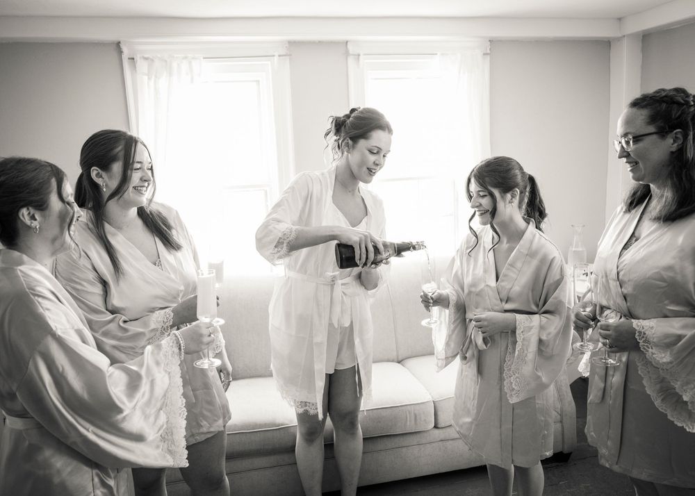Bride opening champagne with bridesmaids in robes during wedding preparations.