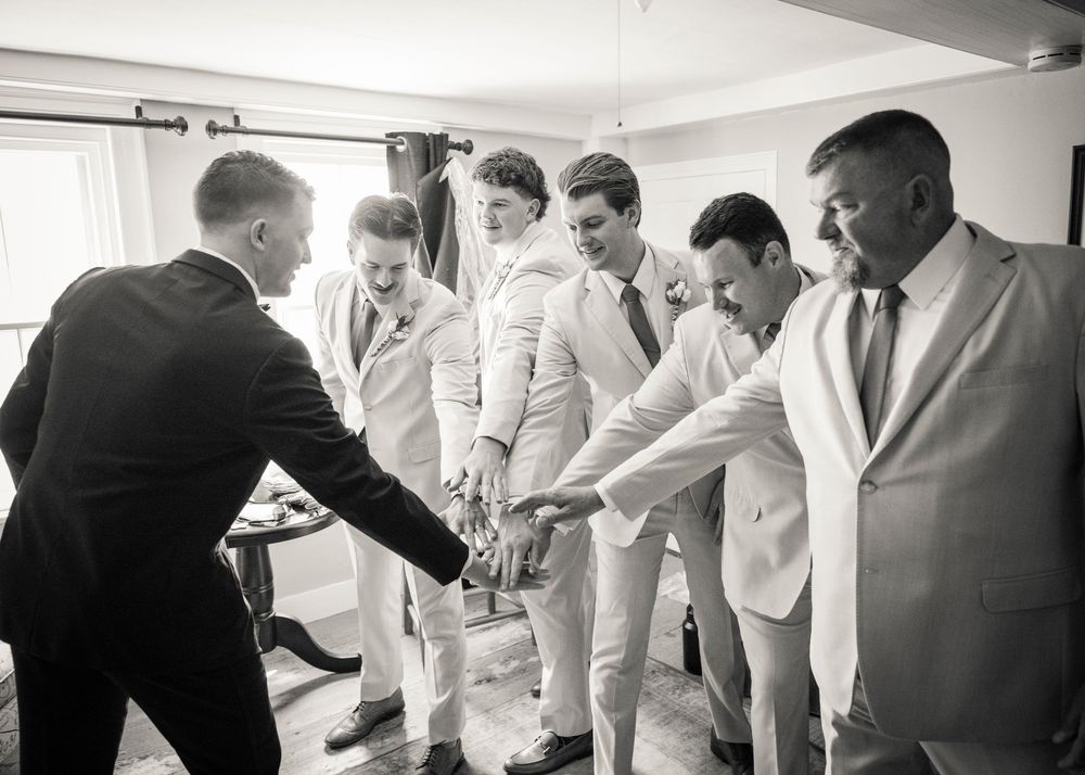 Groomsmen in tan suits celebrating with a group handshake before wedding ceremony in black and white photo.