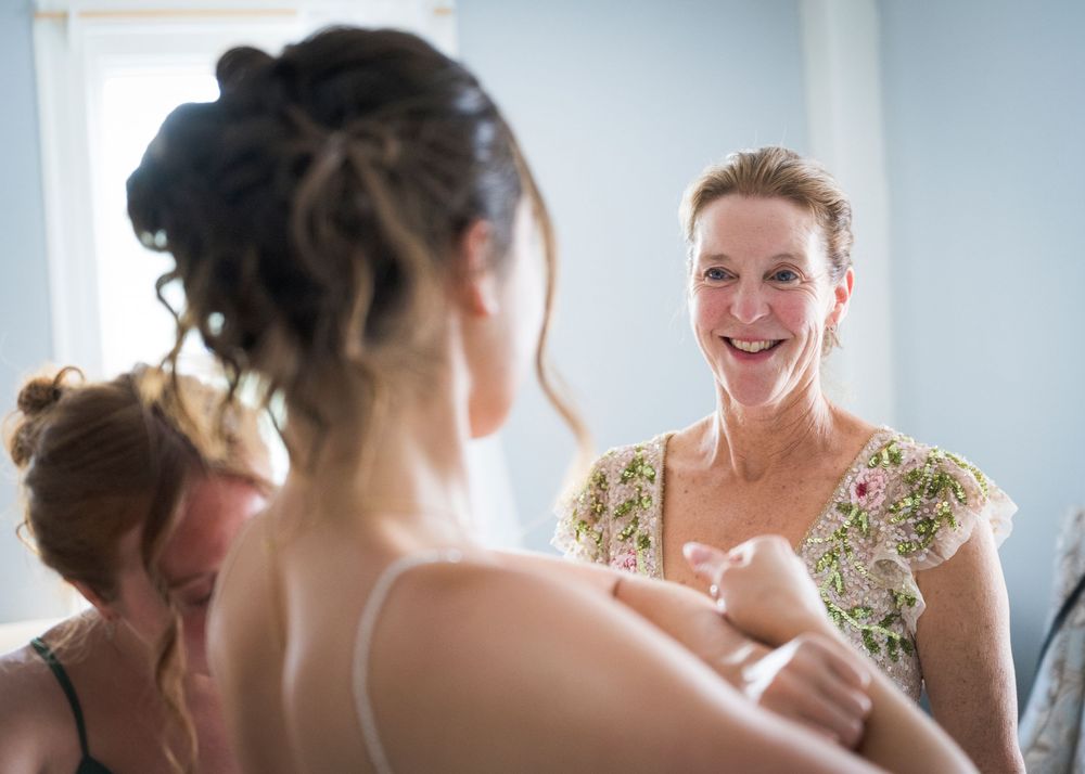 Smiling mother helps bride get dressed in a bright room before the wedding ceremony.