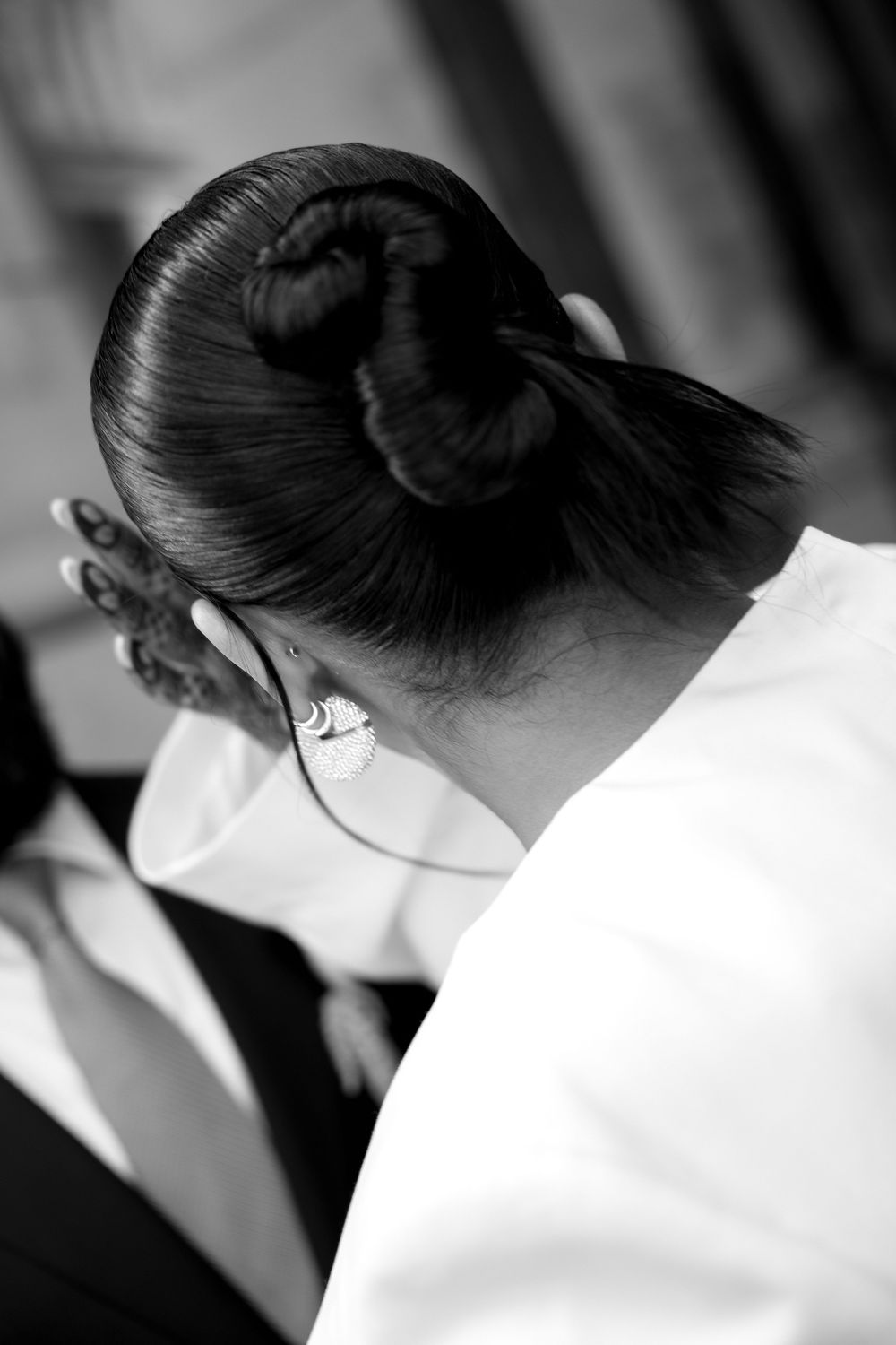 Black and white photo of a woman with an elegant hair bun updo, wearing a pearl earring and white dress.