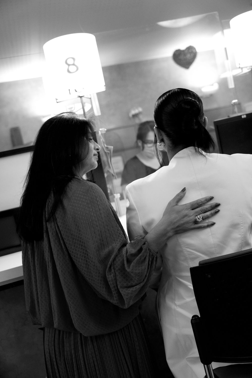 Black and white photo of two women sharing an intimate moment, one in a white coat, in a softly lit room.