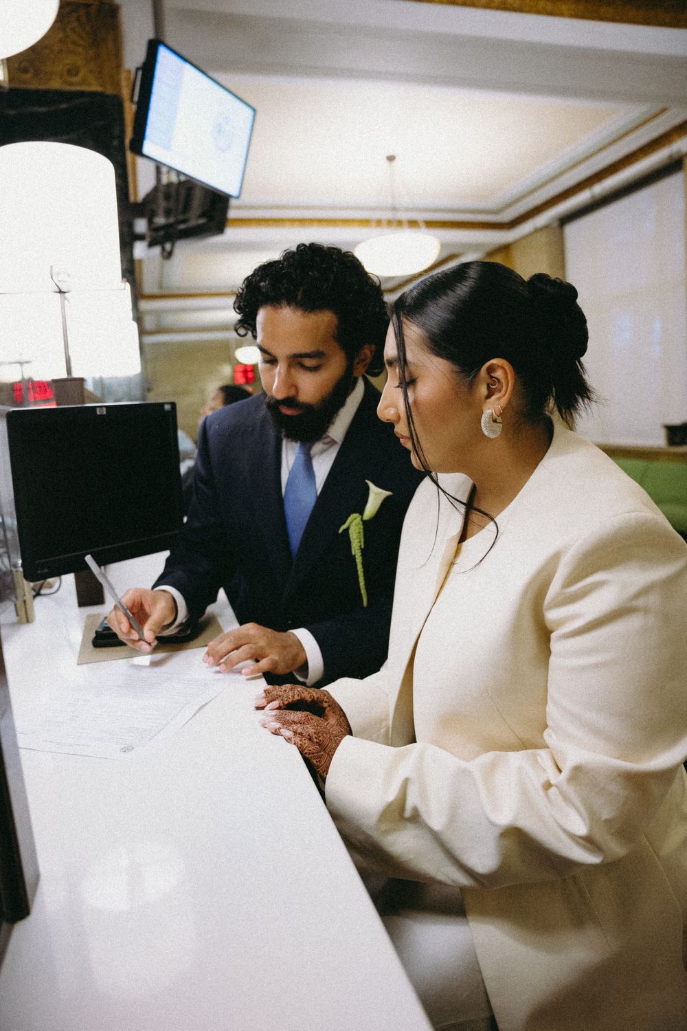 Bride and groom signing wedding documents at a courthouse registry office counter.