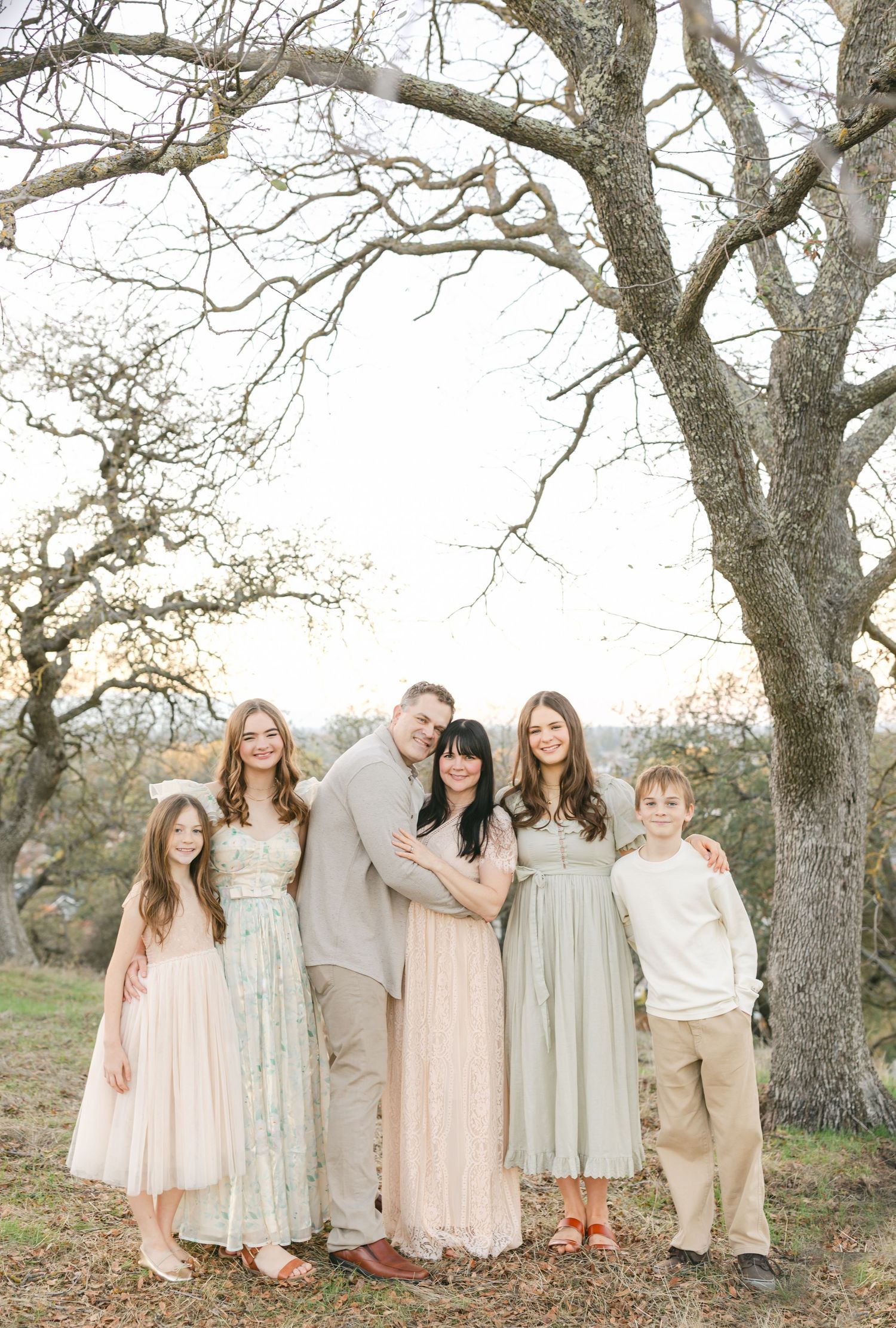 A wedding party poses together under blooming spring trees on a grassy hillside during golden hour.