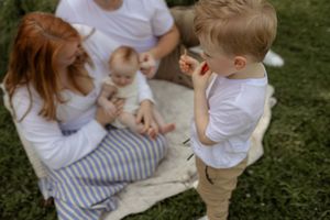 A young family with a baby and toddler enjoying a picnic on green grass outdoors on a sunny day.