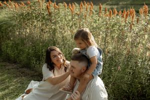 A joyful family shares a tender moment together outdoors against tall ornamental grasses in warm sunlight.