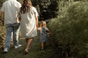 Family walking together on a garden path surrounded by lush greenery on a sunny afternoon.