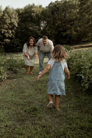 Family in casual clothing picking berries together in a lush green field on a sunny afternoon.