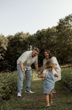 A happy family with two parents laughing and bending down to greet their young daughter in a lush green garden.