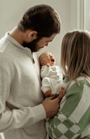 Tender moment with a newborn baby in white clothing being held by parents wearing cozy sweaters.