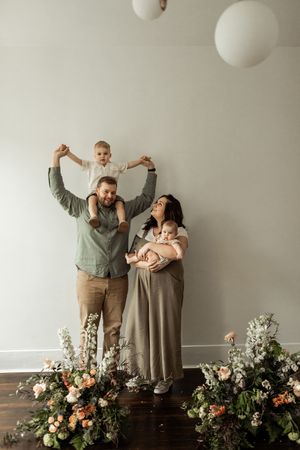 A group of people stand together against a white wall with floral arrangements at their feet.