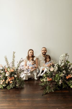 A family poses together on a wooden surface decorated with lush floral arrangements featuring peach and white blooms.