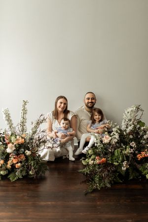 A series of five photos showing a family sitting against a gray wall with floral arrangements on a dark wooden surface.