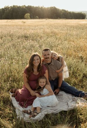 Family of four smiling together on a blanket in a golden sunlit meadow during a warm outdoor portrait session.