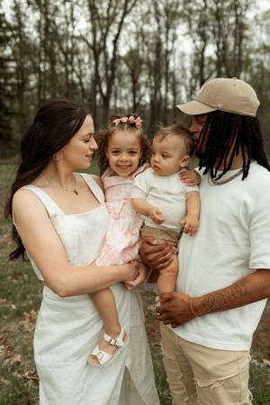 A family shares a tender outdoor moment together in white outfits against a wooded backdrop.