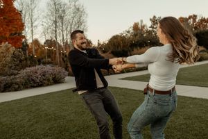 A playful couple and their brown dog dance and laugh together in a grassy field at sunset.