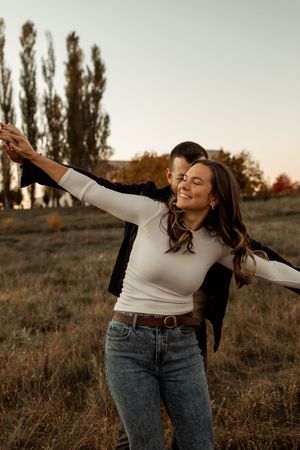 A person in a white sweater and jeans dances joyfully in a golden autumn field at sunset.