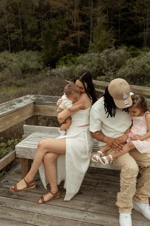 A family sits together on wooden deck steps surrounded by lush forest scenery on a warm day.