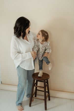 Parent and child share a tender moment while playing together on a wooden stool against a neutral wall.