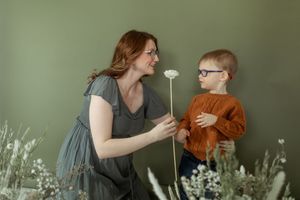 A couple embraces tenderly in front of a green wall with delicate white flowers in the foreground.